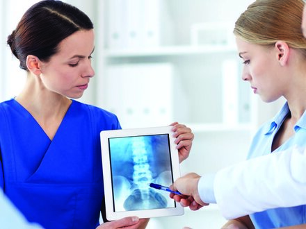 A group of healthcare professionals review an X-ray on a tablet